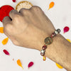 Hand wearing a beaded bracelet with decorative elements on a white background