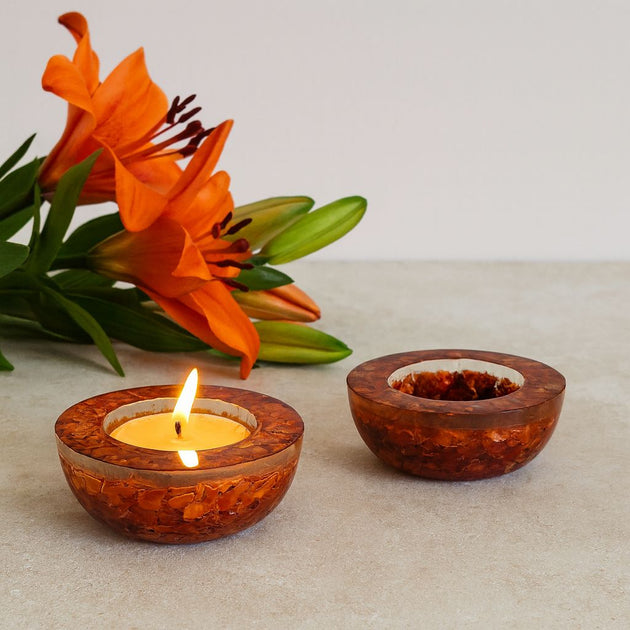 Wooden candle holders with a lit candle and an orange flower on a light surface