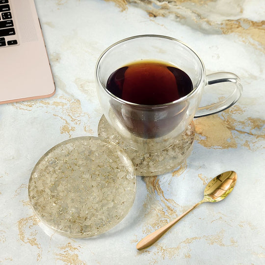 Clear glass mug with dark liquid on a marble surface with a laptop and gold spoon.