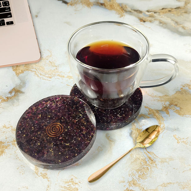 Glass mug with dark liquid on purple stone coasters on a marble surface with a laptop.