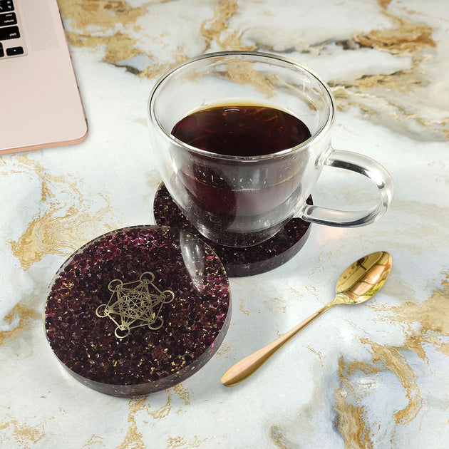 Clear glass mug with dark liquid on a decorative coaster on a marble surface with a laptop.