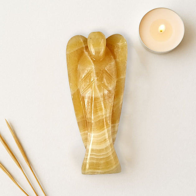 Decorative angel sculpture made of a golden stone material on a light background with a candle and incense sticks.