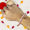 Hand wearing a beaded rakhi with colorful petals on a white background