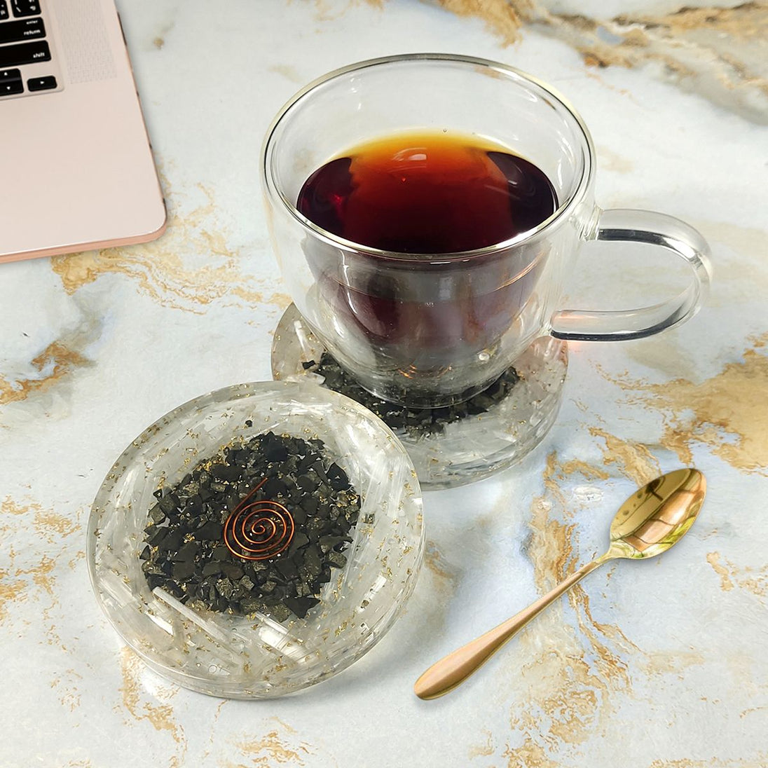 Clear glass cup with black tea on a Coaster surface with a laptop.