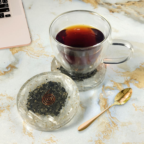 Clear glass cup with black tea on a Coaster surface with a laptop.