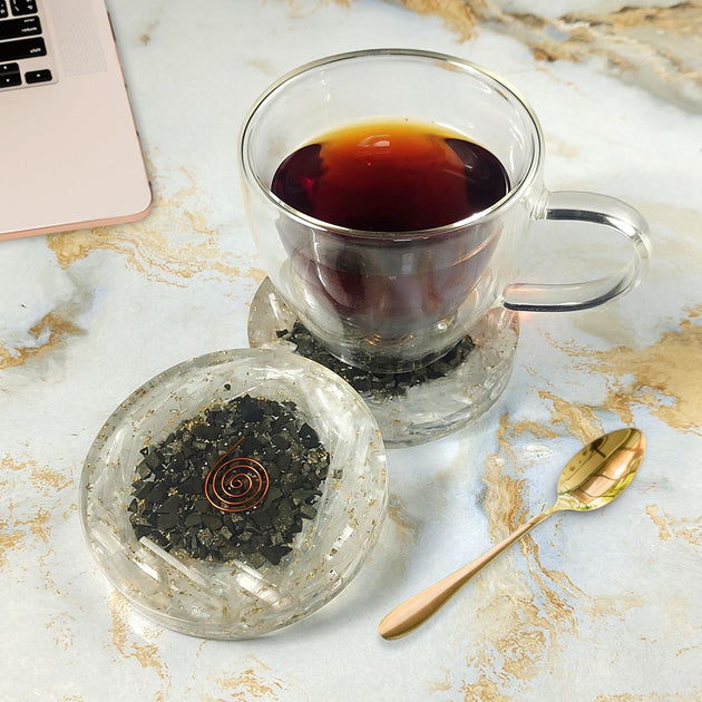 Clear glass cup with black tea on a Coaster surface with a laptop.