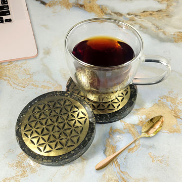 Clear glass mug with dark liquid on decorative coasters on a marble surface with a laptop.