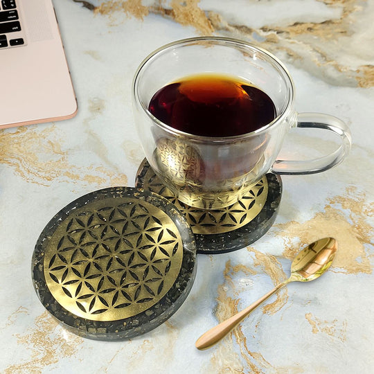 Clear glass mug with dark liquid on decorative coasters on a marble surface with a laptop.