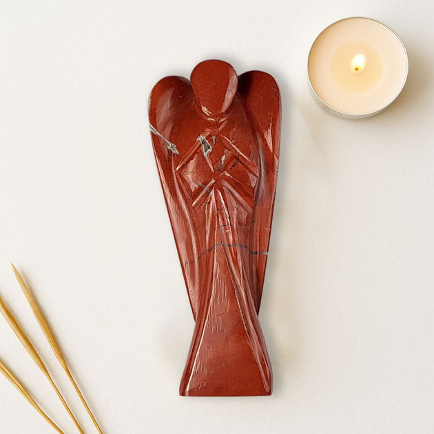 Handcrafted red stone sculpture on a white surface with a candle and incense sticks.
