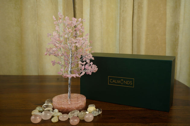 pink color Rose Quartz Crystal Tree with orgonite base and surrounded by pebbles with a green box behind of calminds