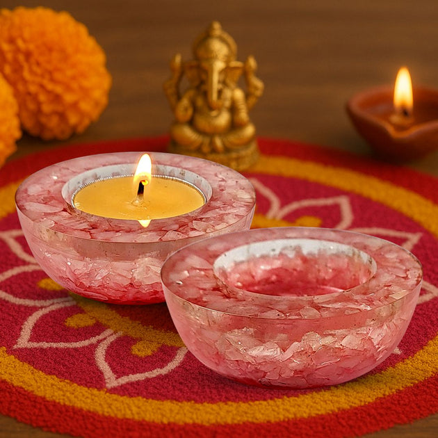 Pink crystal candle holders with lit candles on a decorative mat with a statue in the background