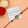 Decorative Rakhi with Om pendant on a card, surrounded by red powder and rice on a peach background