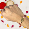 Hand wearing a rakhi with decorative elements on a white background with colored petals.