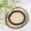 Brown beaded smoky quartz crystal bracelet on a wooden slice with white flowers in the background 