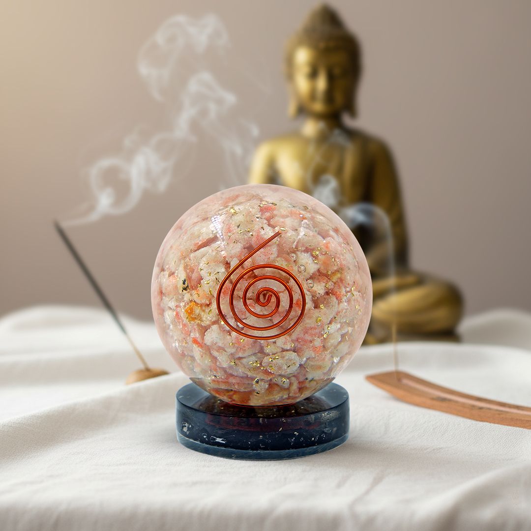 sunstone orgonite ball with a spiral design in front of a Buddha statue on a white surface.