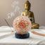 sunstone orgonite ball with a spiral design in front of a Buddha statue on a white surface.