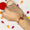 Hand wearing a beaded rakhi with red and white powders and petals in the background