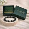 Black beaded bracelet on a round wooden platform with 'CALMINDS' branded box in the background.