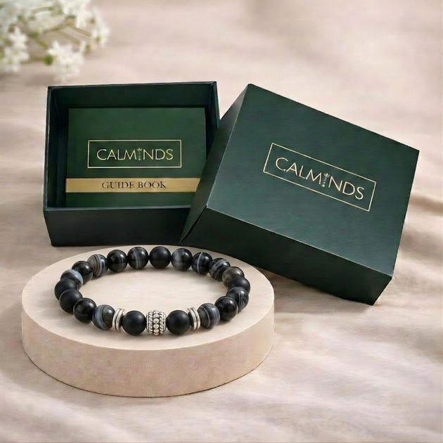 Black beaded bracelet on a round wooden platform with 'CALMINDS' branded box in the background.