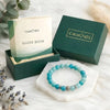 Turquoise beaded bracelet on a white stand with 'Calminds' branded box and guidebook in the background.