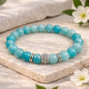 Turquoise beaded bracelet with a silver charm on a stone surface with flowers.