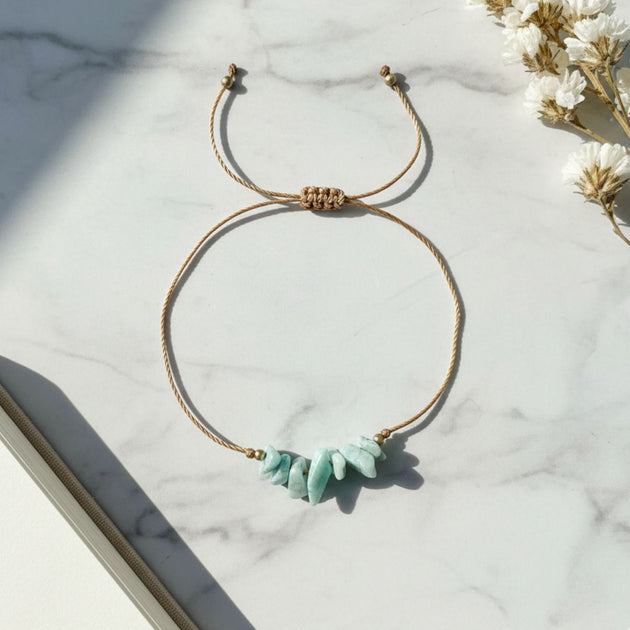 golden thread bracelet with green stones on a marble surface with white flowers.