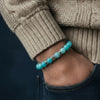 Turquoise beaded bracelet on a wrist with a beige sweater and dark background