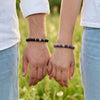 Two people holding hands with beaded bracelets against a grassy background