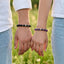 Two people holding hands with beaded bracelets against a grassy background