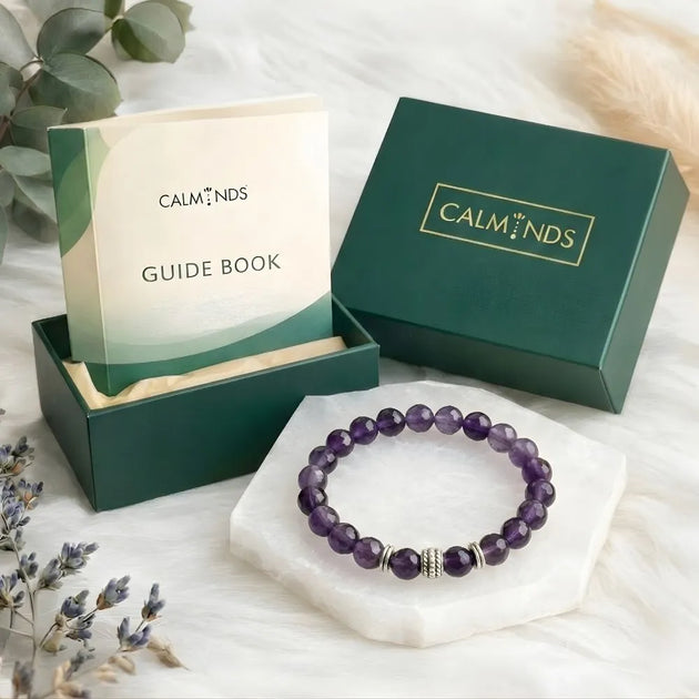 Purple beaded bracelet on a white surface with 'Calminds' packaging and guidebook.
