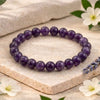 Purple beaded bracelet on a stone surface with flowers