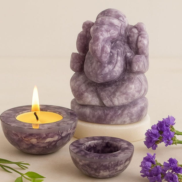 Purple amethyst crystal ganesha and tea light holder with lit candle and purple flowers on a beige background