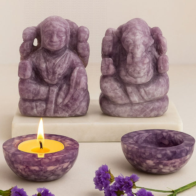 Purple stone statues and candle on a white surface with purple flowers.