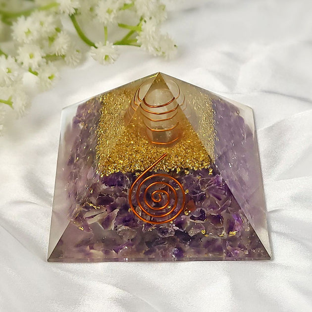 amethyst crystal pyramid with gold and purple elements on a white fabric background