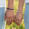 Two people holding hands with beaded bracelets against a blurred natural background