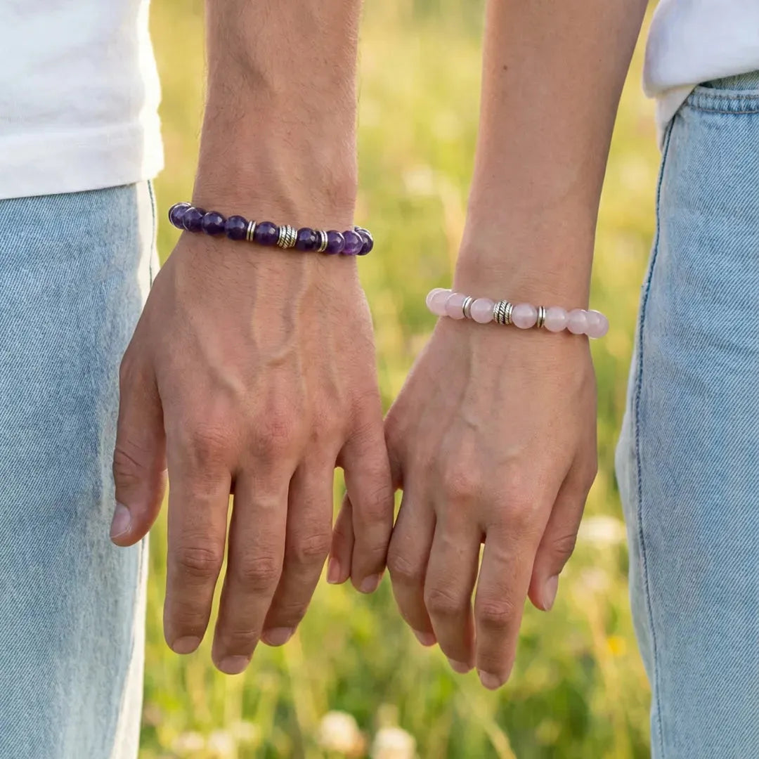 Two people holding hands with beaded bracelets against a blurred natural background