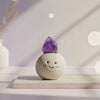 Ceramic smiley face object with a amethyst purple crystal on top against a soft, blurred background