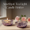 Amethyst tea light candle holder with a lit candle on a surface with flowers in the background.