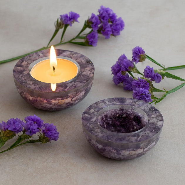 Marble-textured candle holder with a lit candle and purple flowers on a light surface