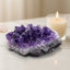 Amethyst crystal cluster on a white surface with a candle in the background