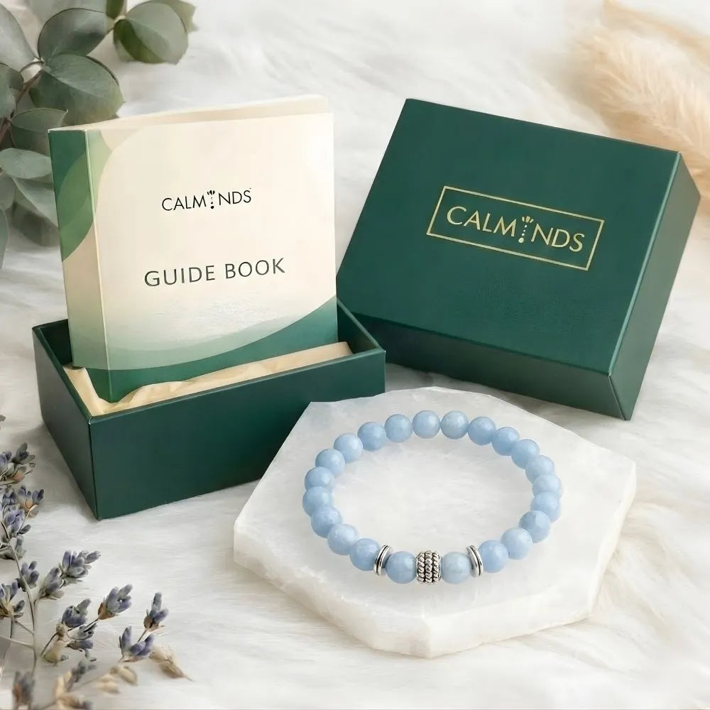Blue beaded bracelet on a white stand with 'Calminds' packaging and guide book in the background.