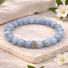 Blue beaded bracelet with a silver clasp on a light wooden surface with flowers.