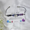 crystal bracelet with butterfly charm on a card detailing benefits, displayed on a white fabric background.
