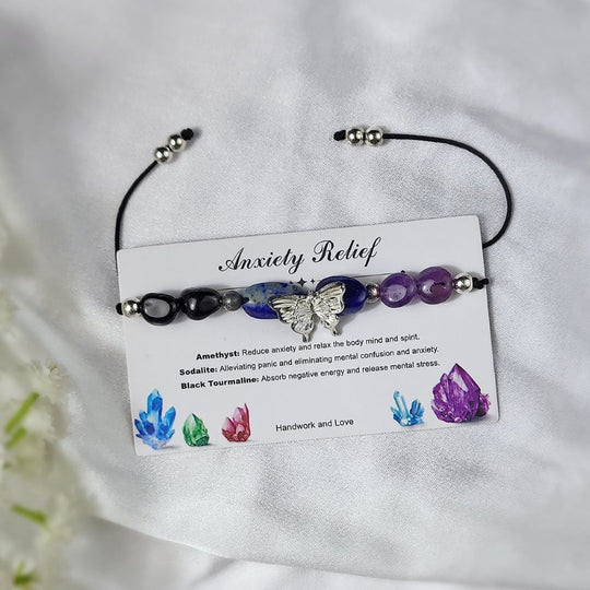 crystal bracelet with butterfly charm on a card detailing benefits, displayed on a white fabric background.