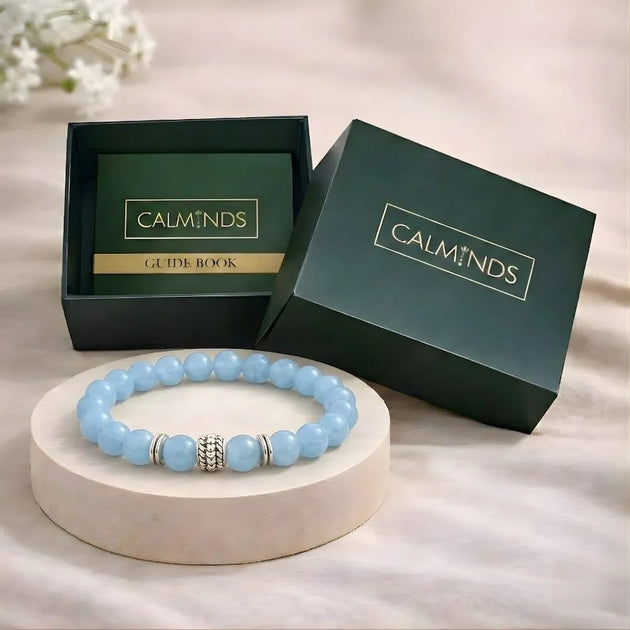Blue beaded bracelet with silver accents on a white stand, next to an open green box with 'CALMINDS' branding.