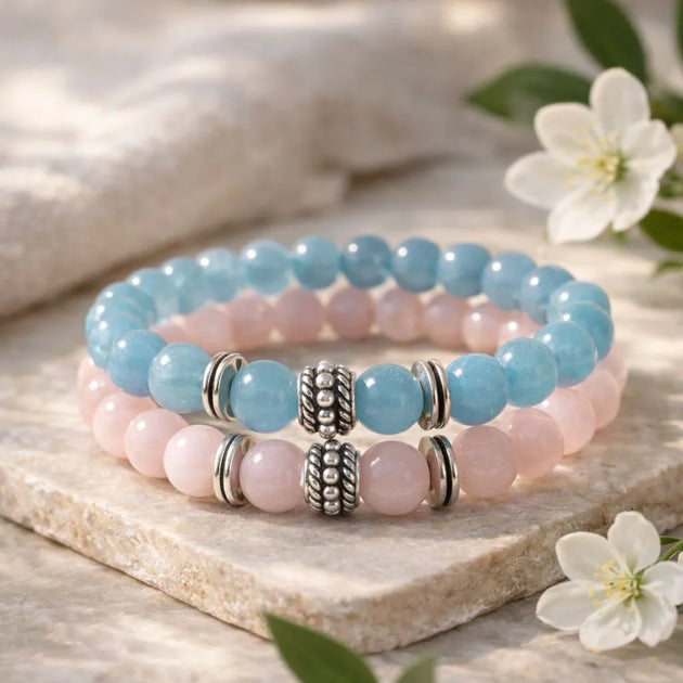 Stack of pink and blue beaded bracelets with silver beads on a stone surface with flowers.