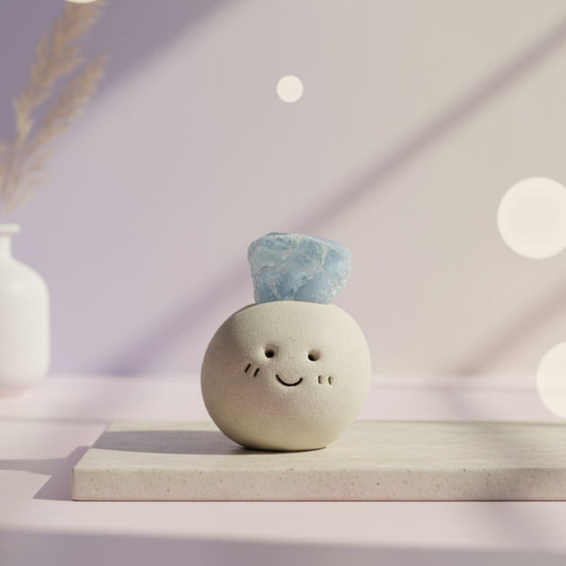 Ceramic round ball with a smiling face and blue aquamarine crystal on top placed on a white surface with soft lighting