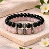 Two beaded bracelets with black and pink beads on a wooden surface with flowers.