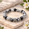 Beaded bracelet with black and white stones on a stone surface with flowers.