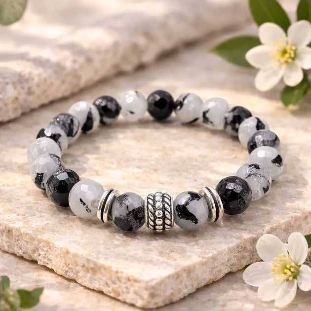 Beaded bracelet with black and white stones on a stone surface with flowers.